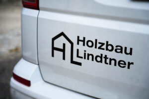 Foto von Beschriftung weißer Hinteransicht eines VW Buses mit Holzbau Lindtner Aufschrift