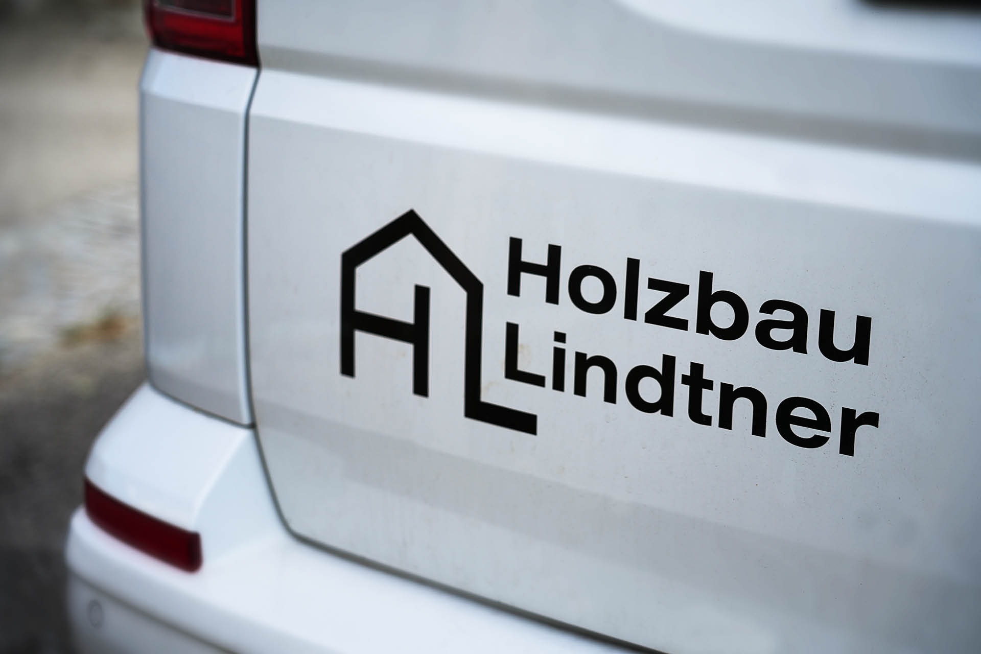 Foto von Beschriftung weißer Hinteransicht eines VW Buses mit Holzbau Lindtner Aufschrift